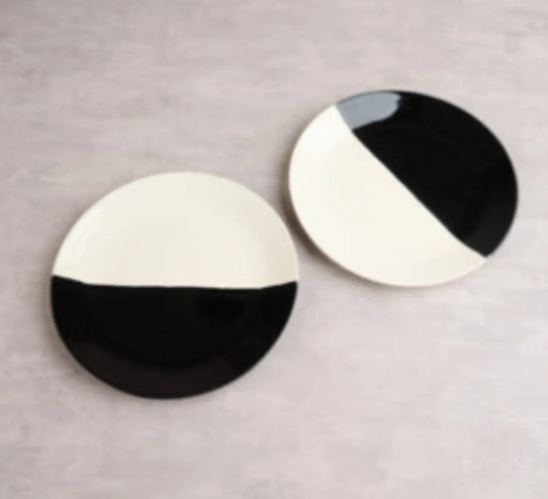 Two modern ceramic dinner plates with a striking black and white geometric design placed on a light grey surface.