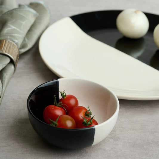 Black and white ceramic bowl filled with cherry tomatoes beside monochrome stoneware plate and napkin – modern kitchenware styling