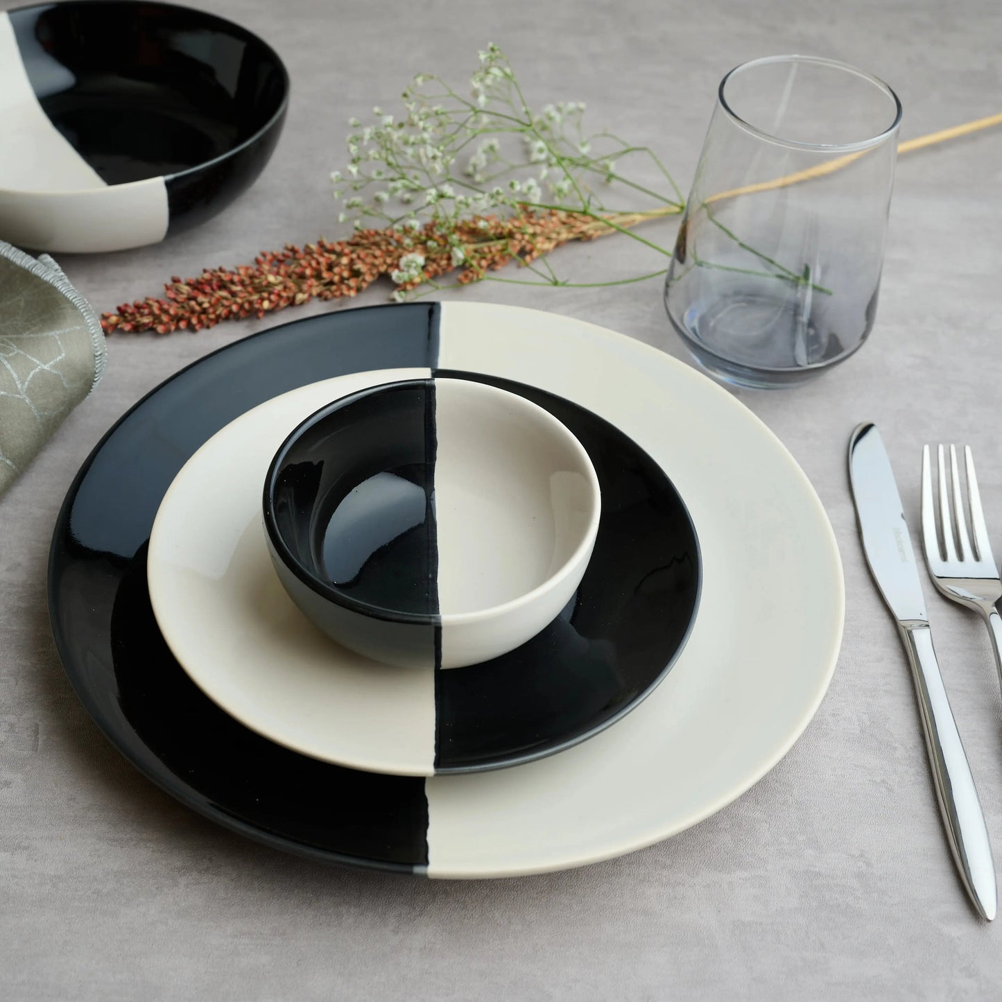 Premium ceramic small bowls with half black half ivory design placed on matching stoneware dinner plate – styled with cutlery and dried flowers