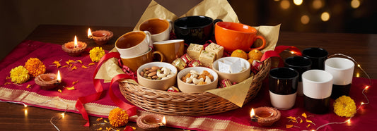 A Diwali gift hamper with Black Carrot mugs, tea cups, and bowls paired with festive sweets